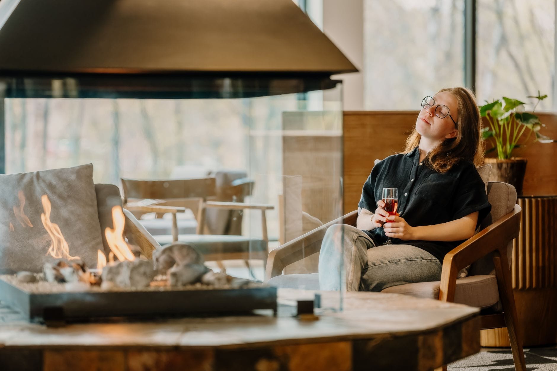 A woman enjoys a quiet moment with a drink by the fireplace in a modern lounge.